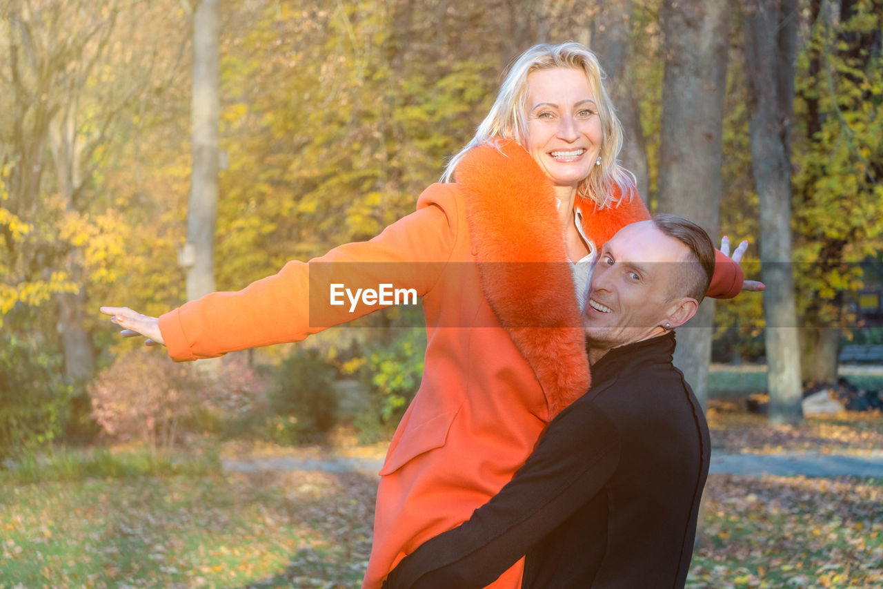 WOMAN WITH ARMS OUTSTRETCHED STANDING ON AUTUMN TREE