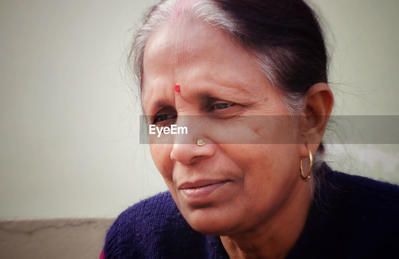 Close-up of mature woman looking away against wall