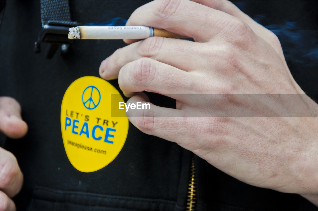 CLOSE-UP OF HAND HOLDING CIGARETTE AGAINST BLURRED BACKGROUND