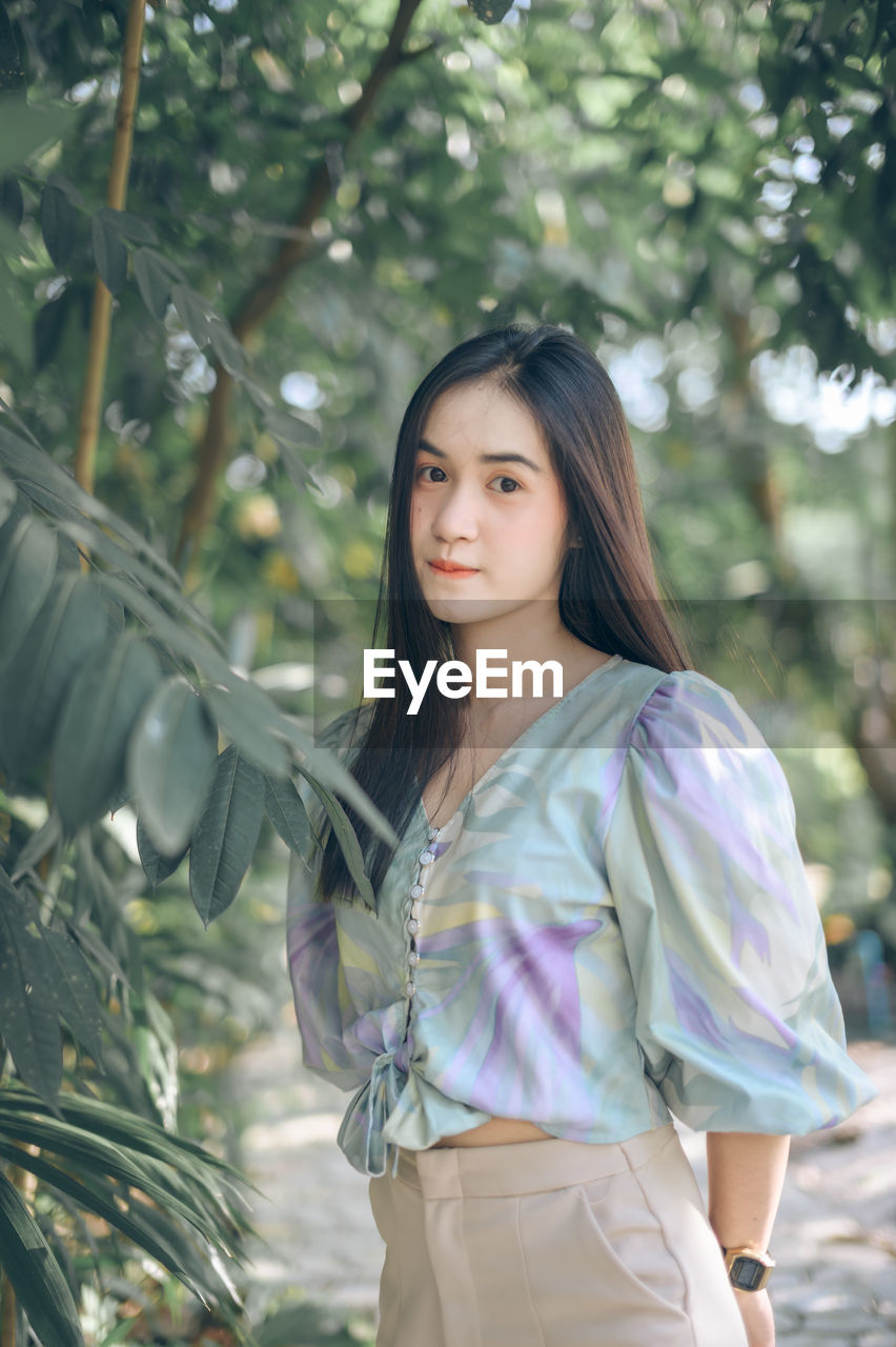 Portrait of young woman standing by trees