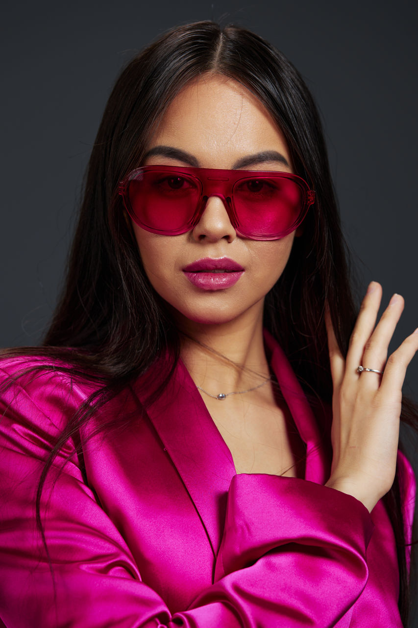 portrait of smiling young woman wearing sunglasses against black background