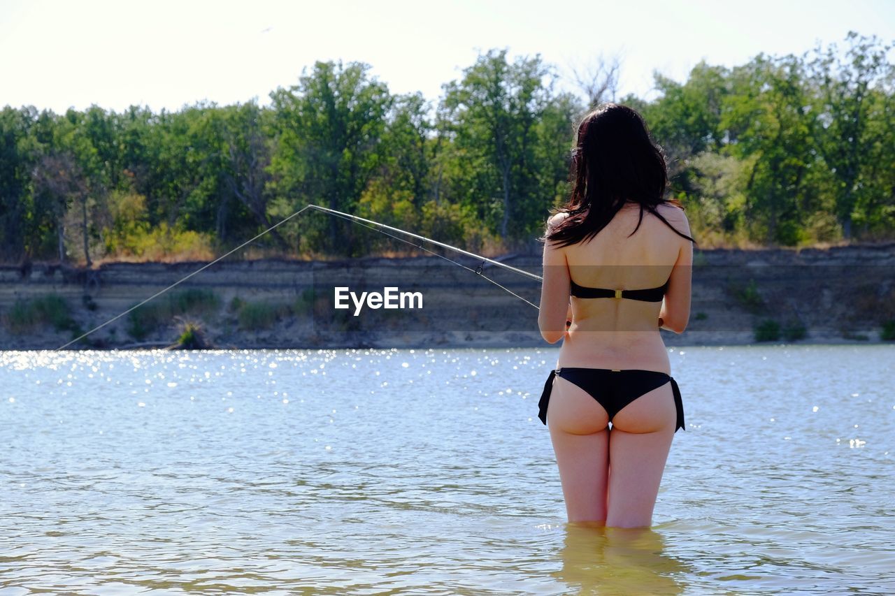 REAR VIEW OF WOMAN STANDING IN SEA