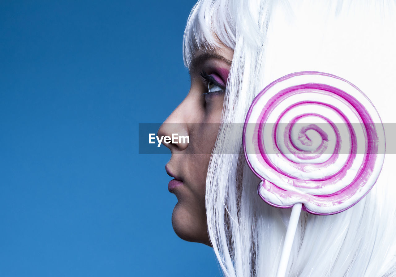 Side view close-up of woman with lollipop against blue background