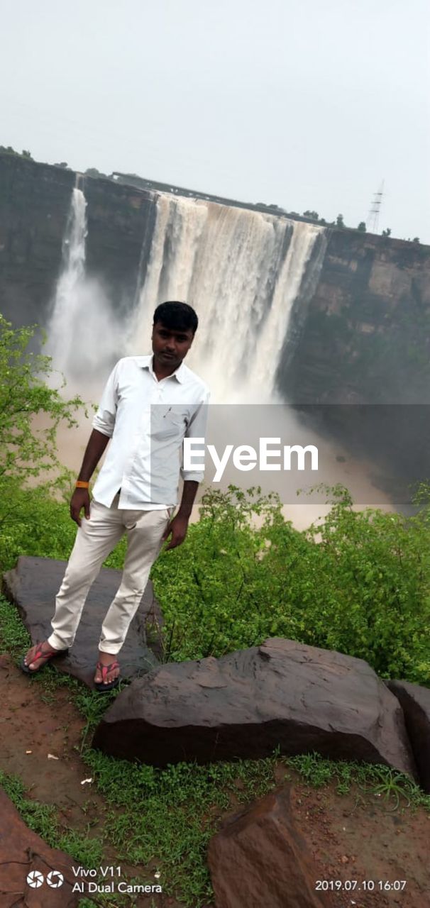 MAN STANDING AGAINST WATERFALL