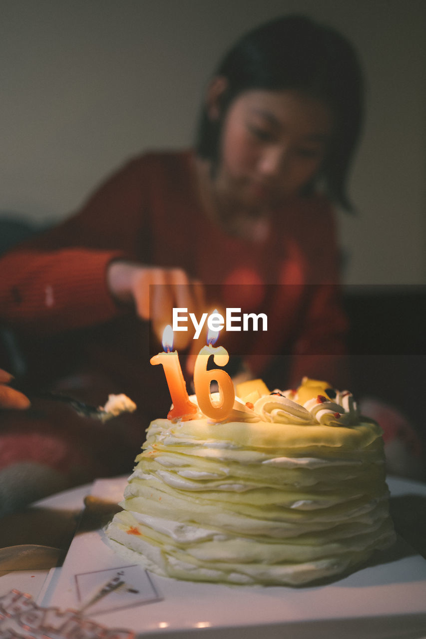 MIDSECTION OF WOMAN WITH ILLUMINATED CANDLES ON CAKE