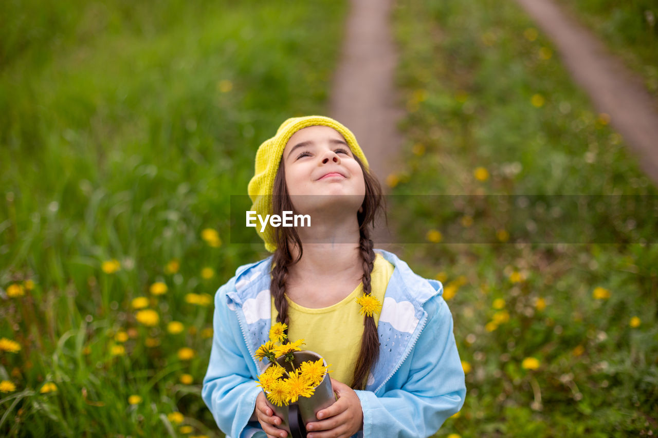 Portrait of a beautiful little girl holds a bouquet of yellow dandelions in a metal mug