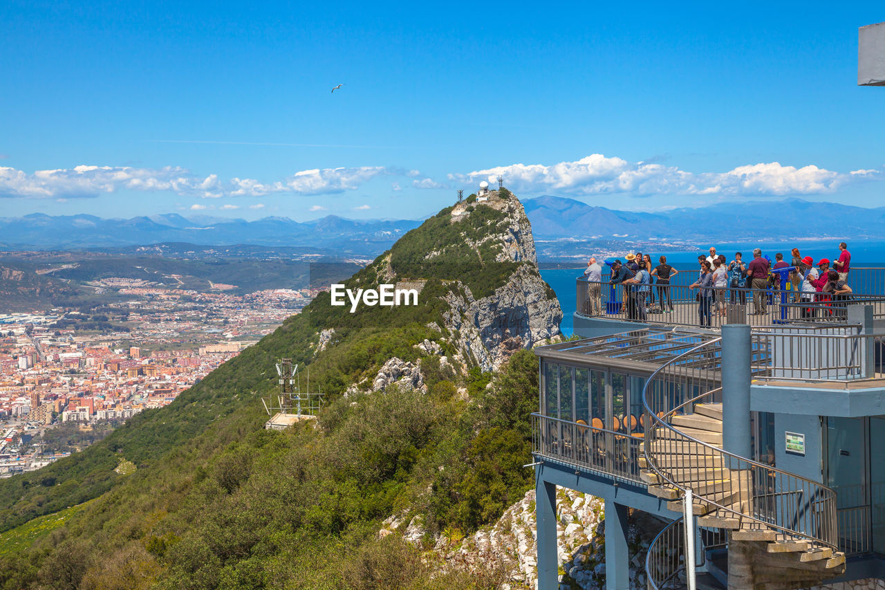 People standing at observation point by mountains against sky during sunny day