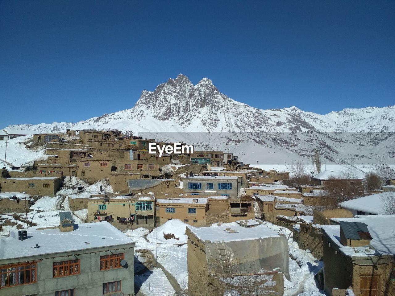 A picture of a snow covered village and mud and clay houses with snow covered mountain in background