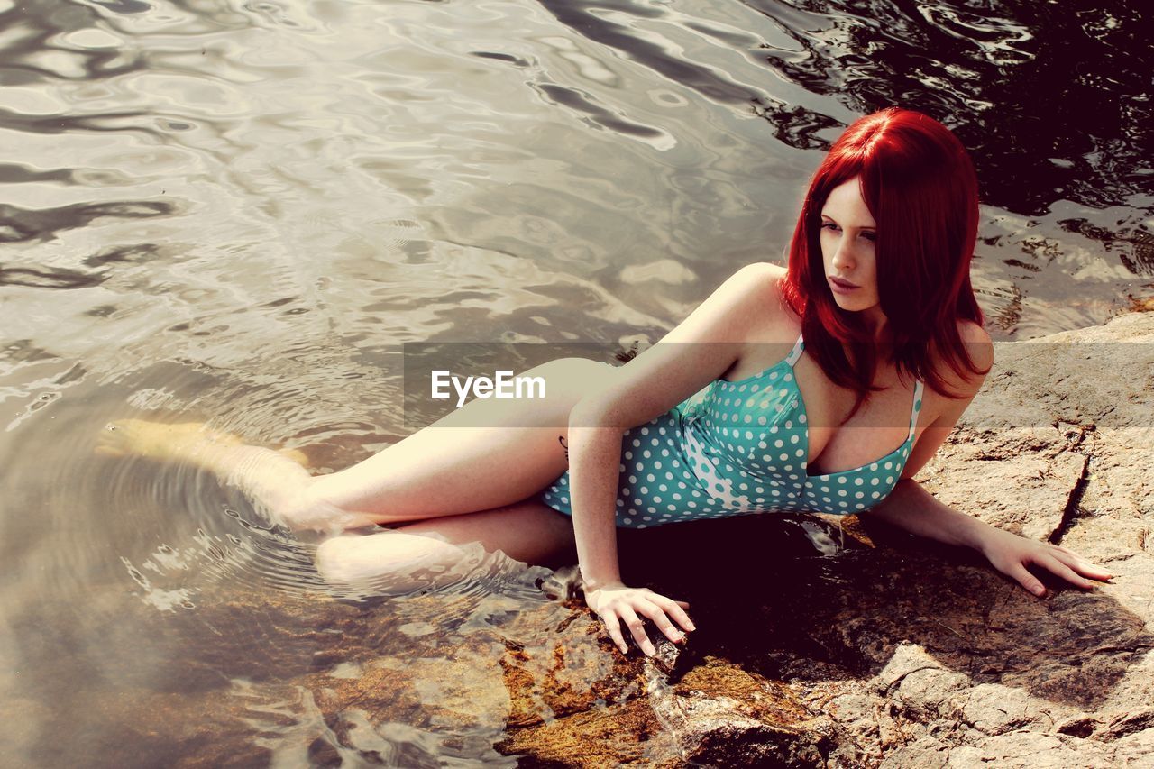 High angle view of young redhead woman reclining on rock at riverbank