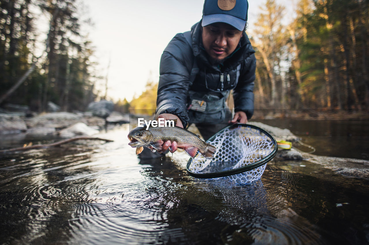 A man catches a trout during a fall morning on a maine river