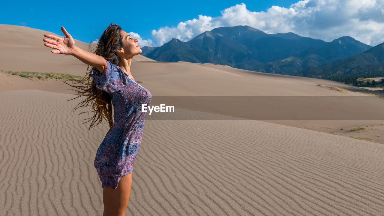 Young woman standing on sand at desert against sky