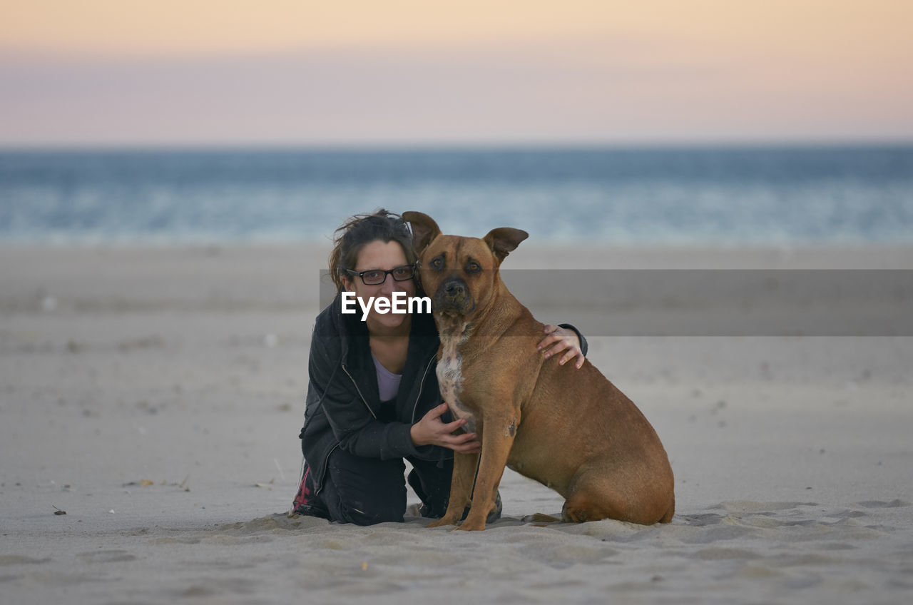 Portrait of woman with dog at beach during sunset