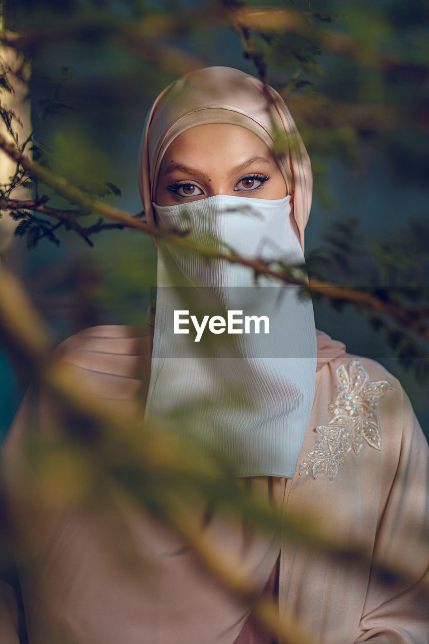 Portrait of veiled woman with white niqab and hijab behind the tree branches