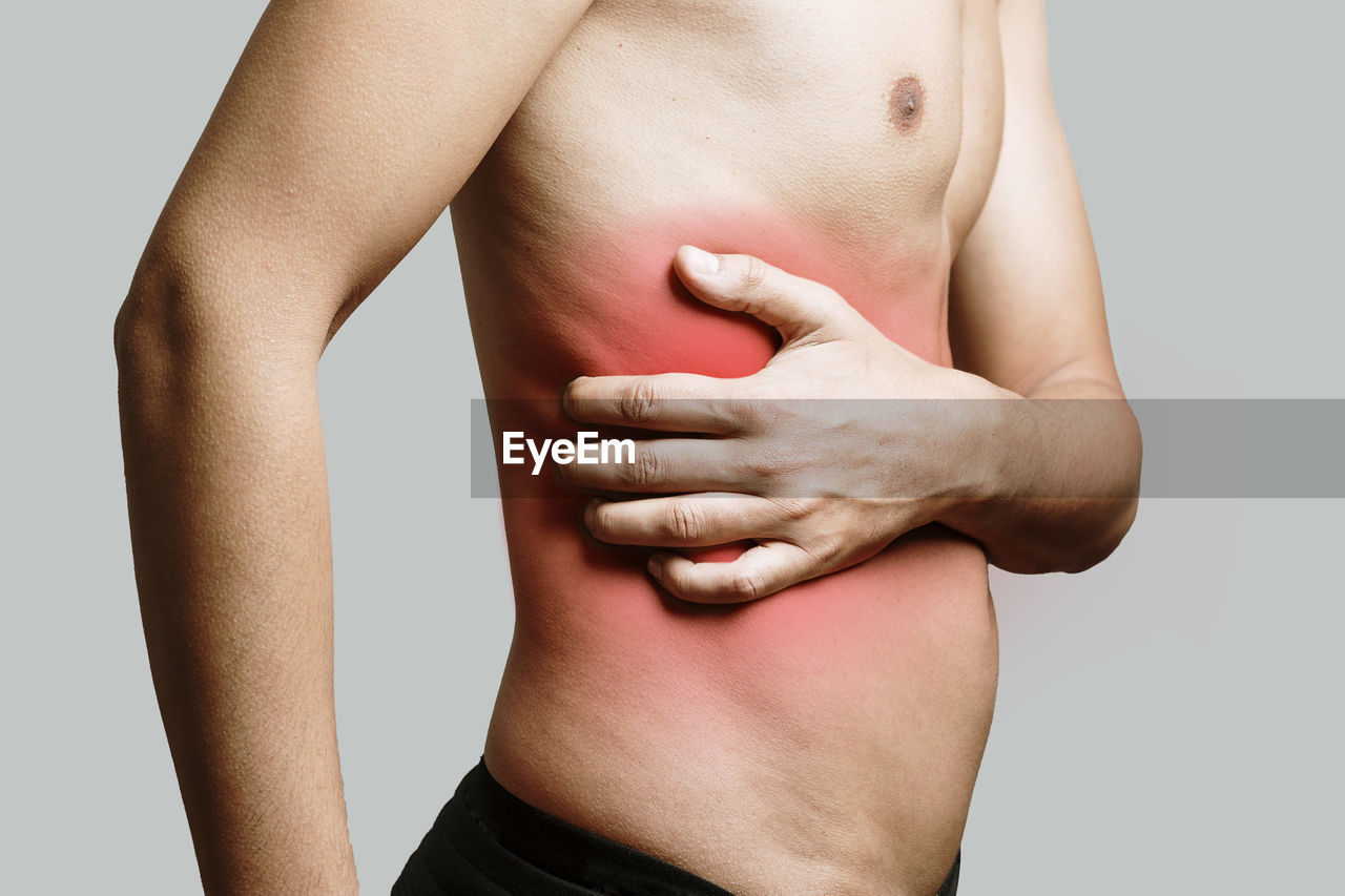 Midsection of shirtless man with red skin against gray background