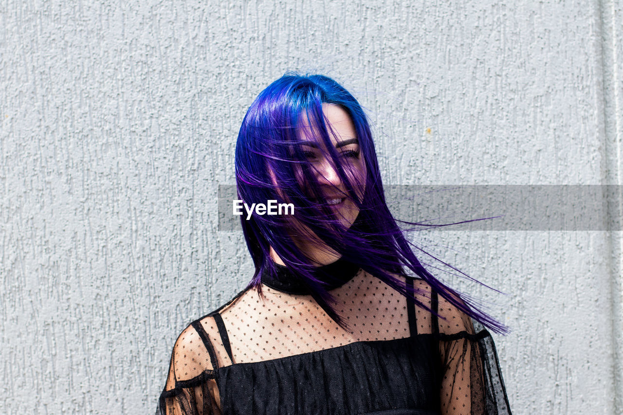 Smiling woman with dyed hair standing against wall