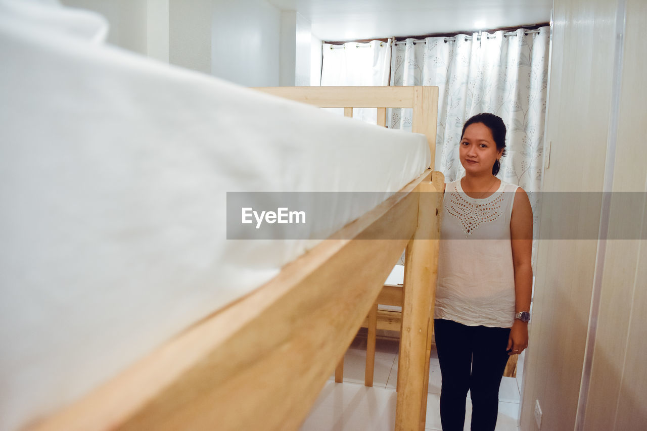 Front view of young woman standing by double deck bed