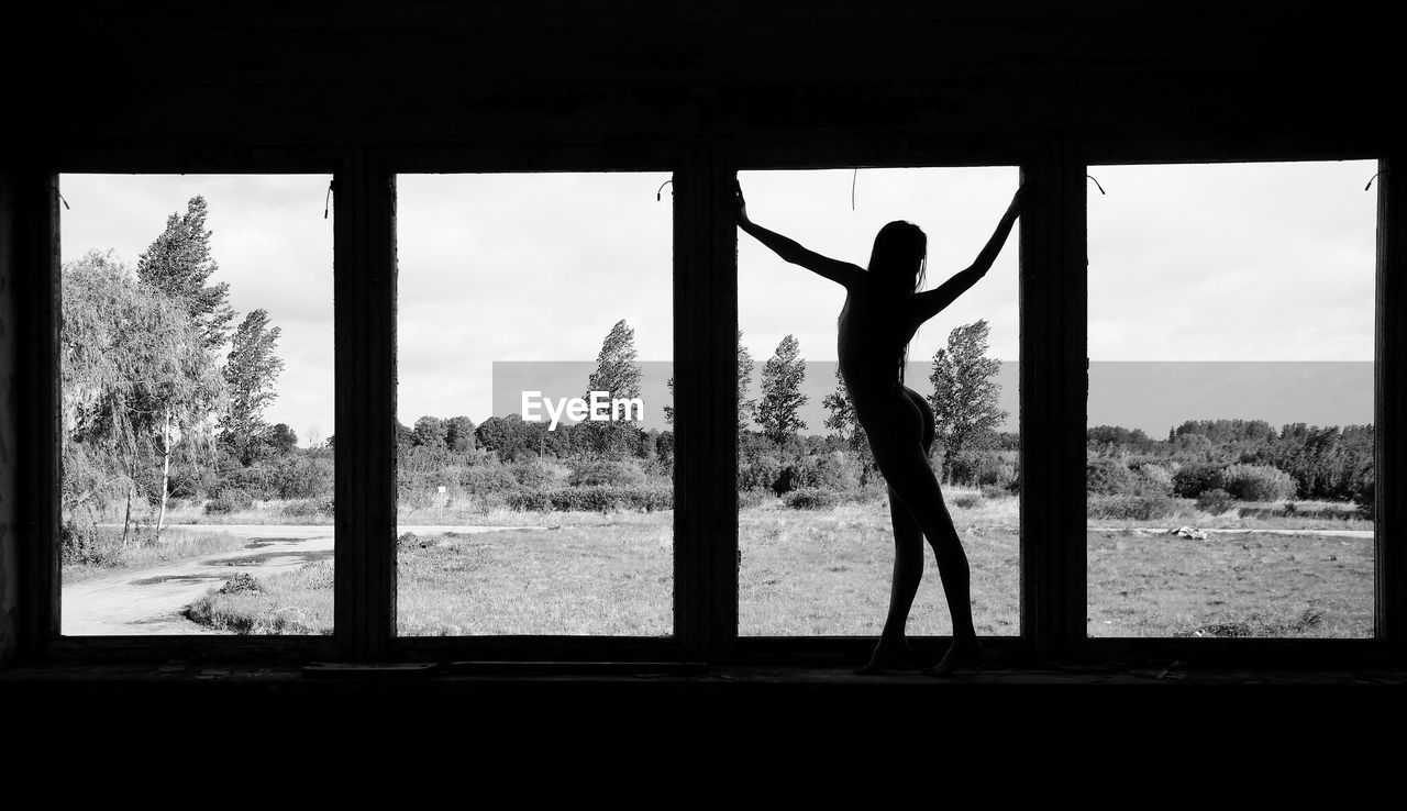 SILHOUETTE MAN STANDING BY WINDOW AGAINST TREES