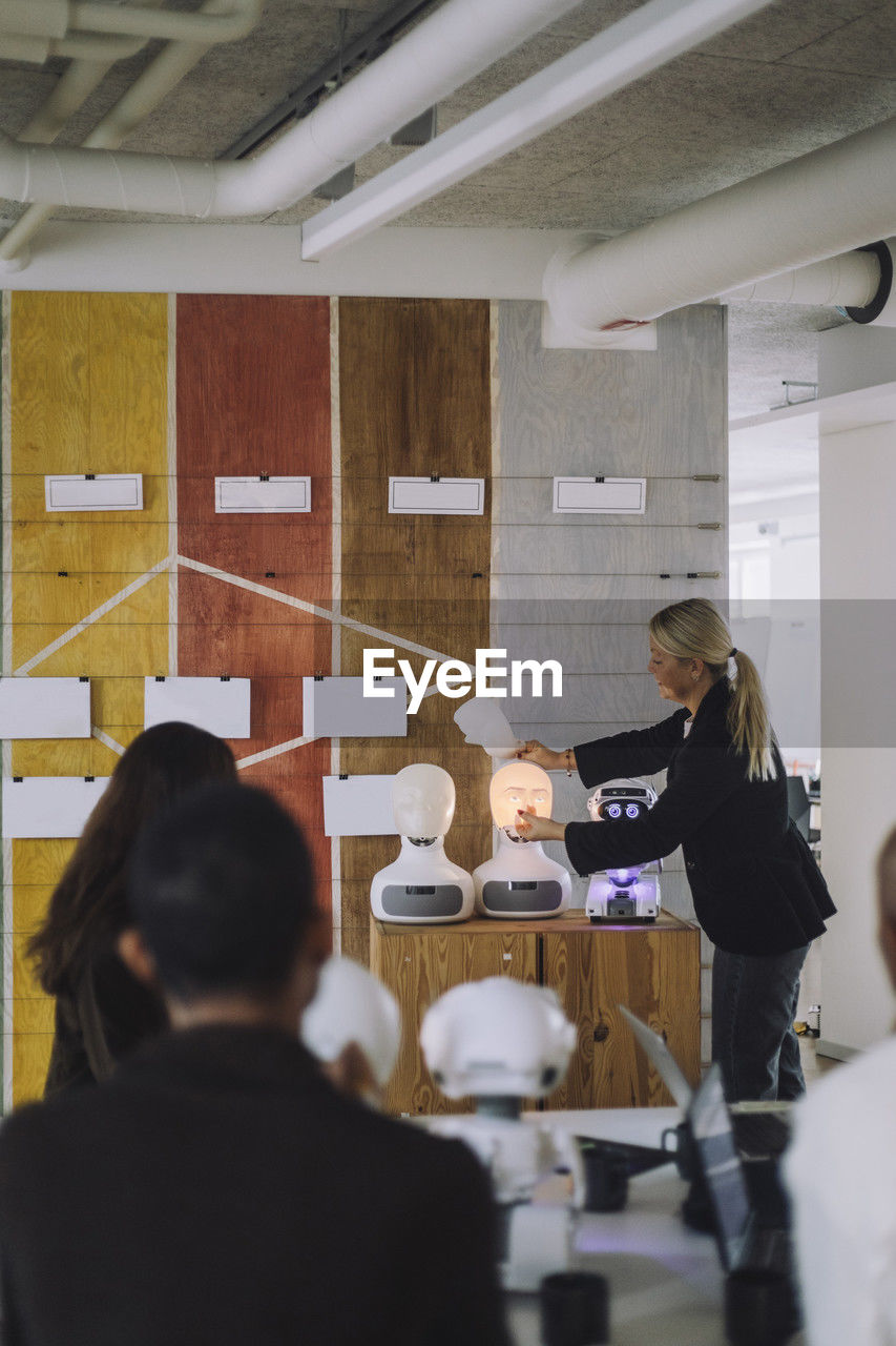 Mature female professor discussing with students over social robot in innovation lab