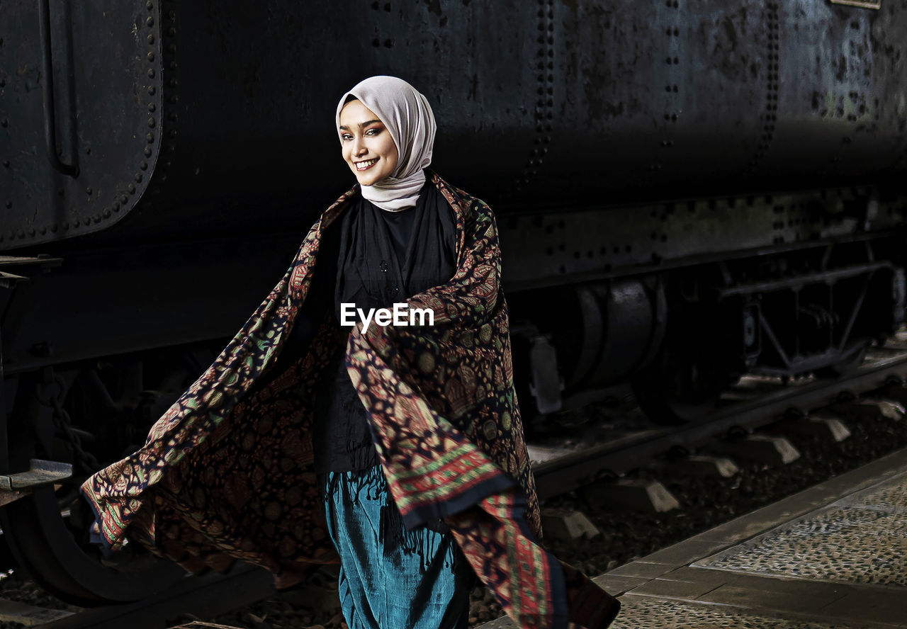 Woman wearing hijab with batik against train