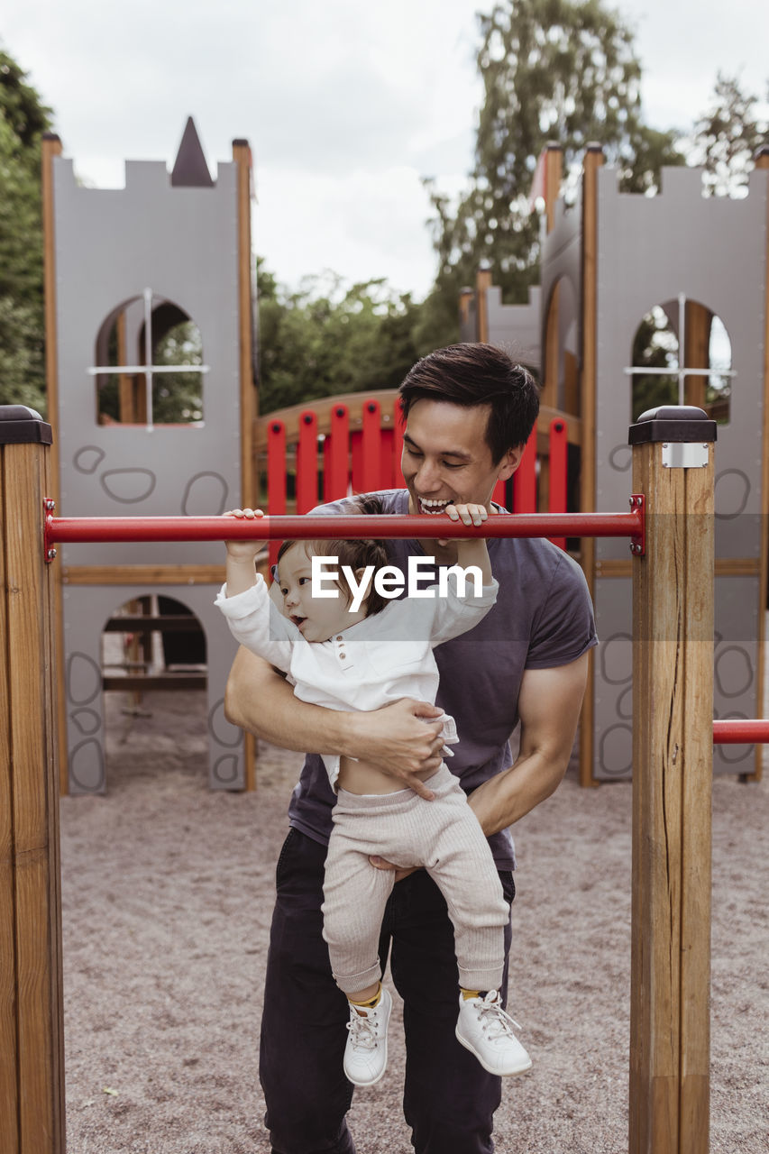 Male toddler with father hanging on monkey bar in playground