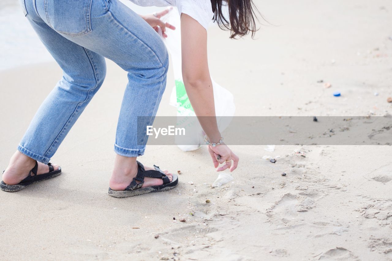 Low section of woman picking garbage at beach