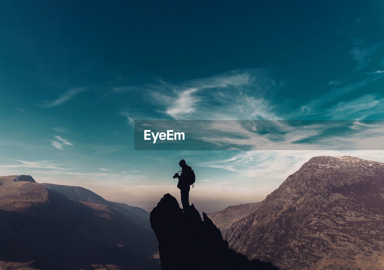 Silhouette man standing on rock against sky