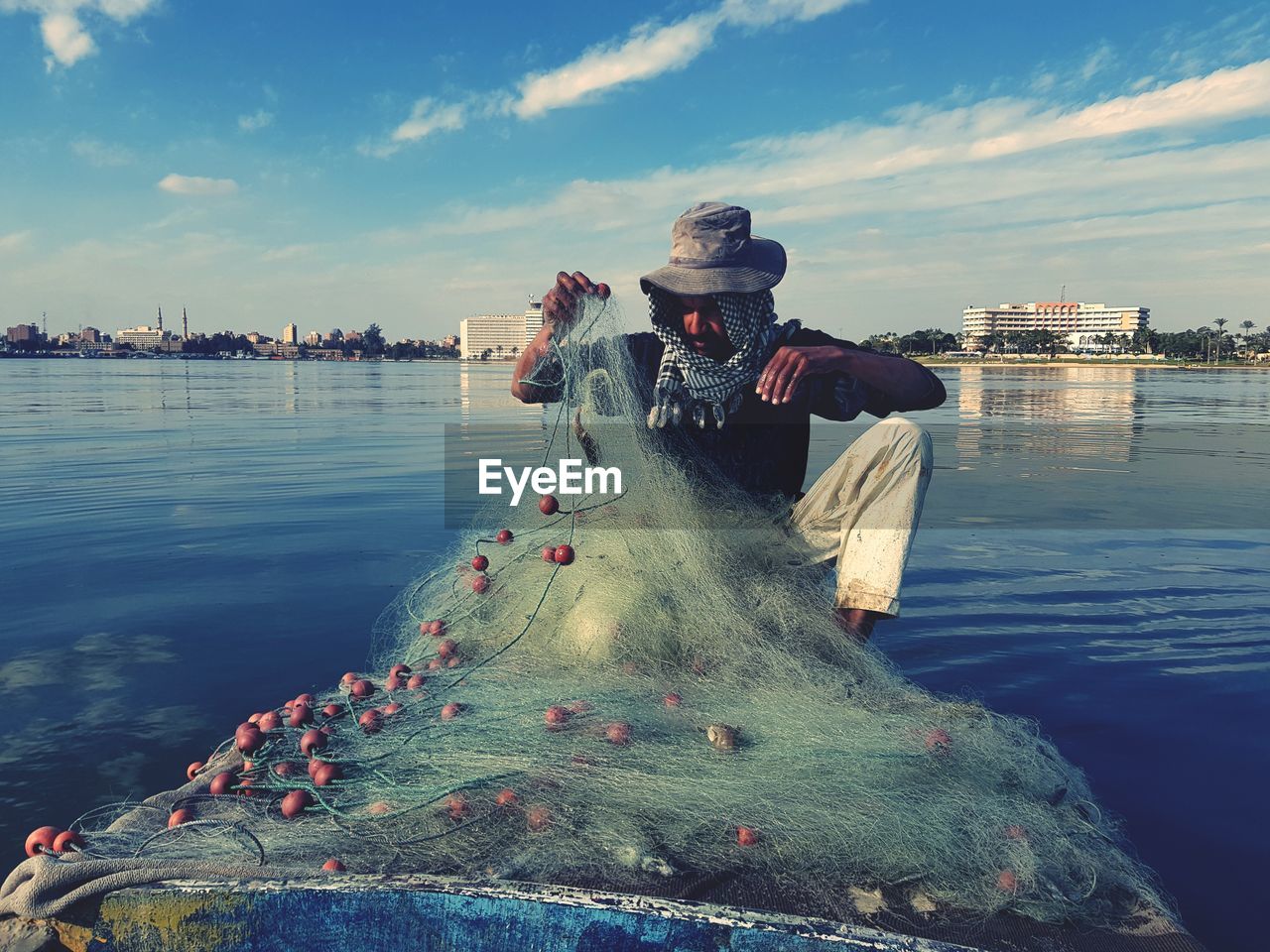 Fisherman with fishing net in boat on lake