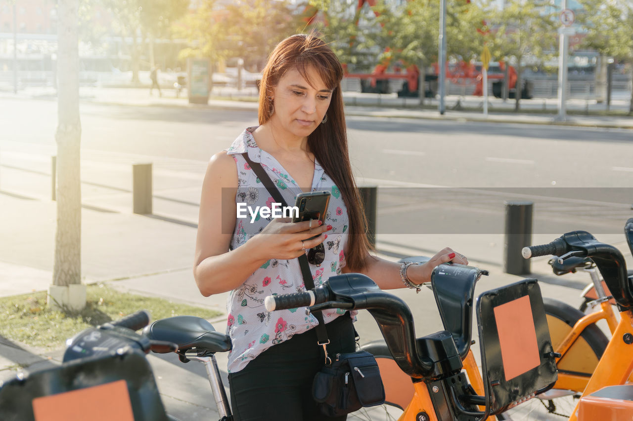 A hispanic woman taking a bicycle in a bike rental platform