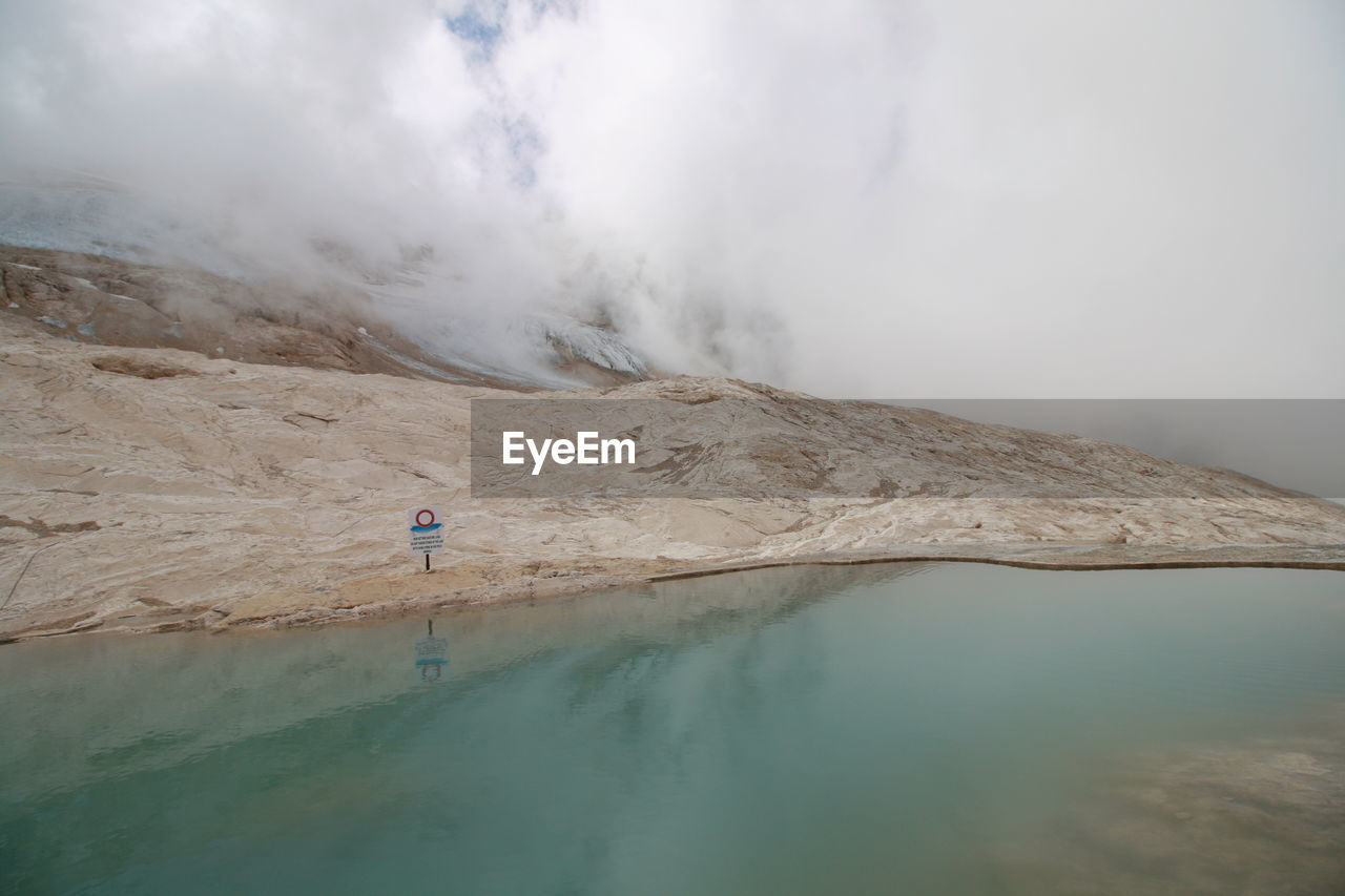 Scenic view of lake by mountain against cloudy sky