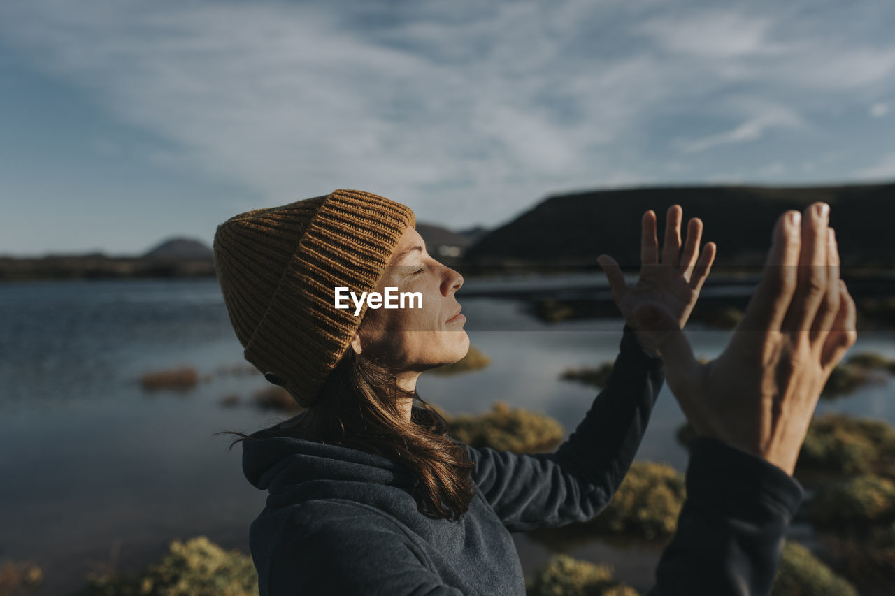 Smiling woman with eyes closed gesturing at lake