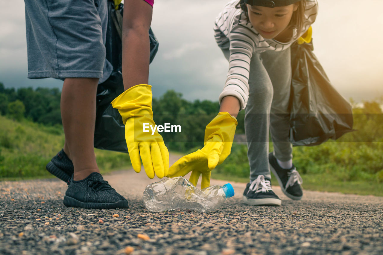 Siblings picking bottles from road against sky