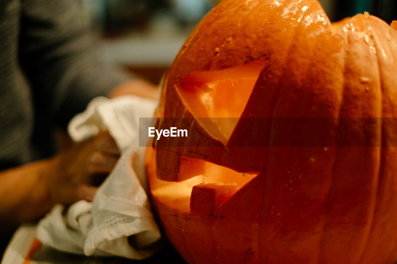 Cropped hands of person carving pumpkin on table at home