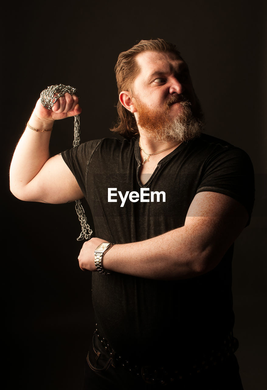 Mid adult man holding chain while standing against black background