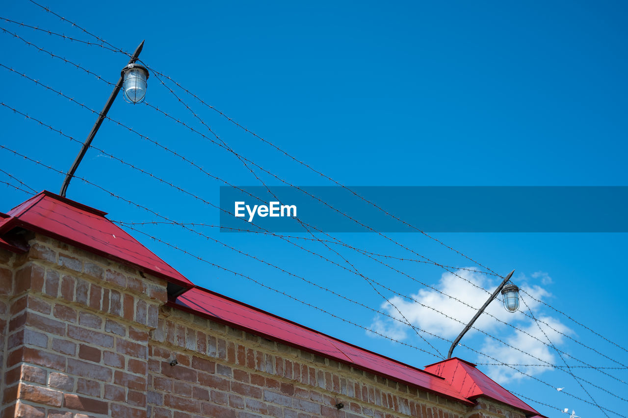 LOW ANGLE VIEW OF POWER LINES AGAINST BUILDING AGAINST CLEAR BLUE SKY