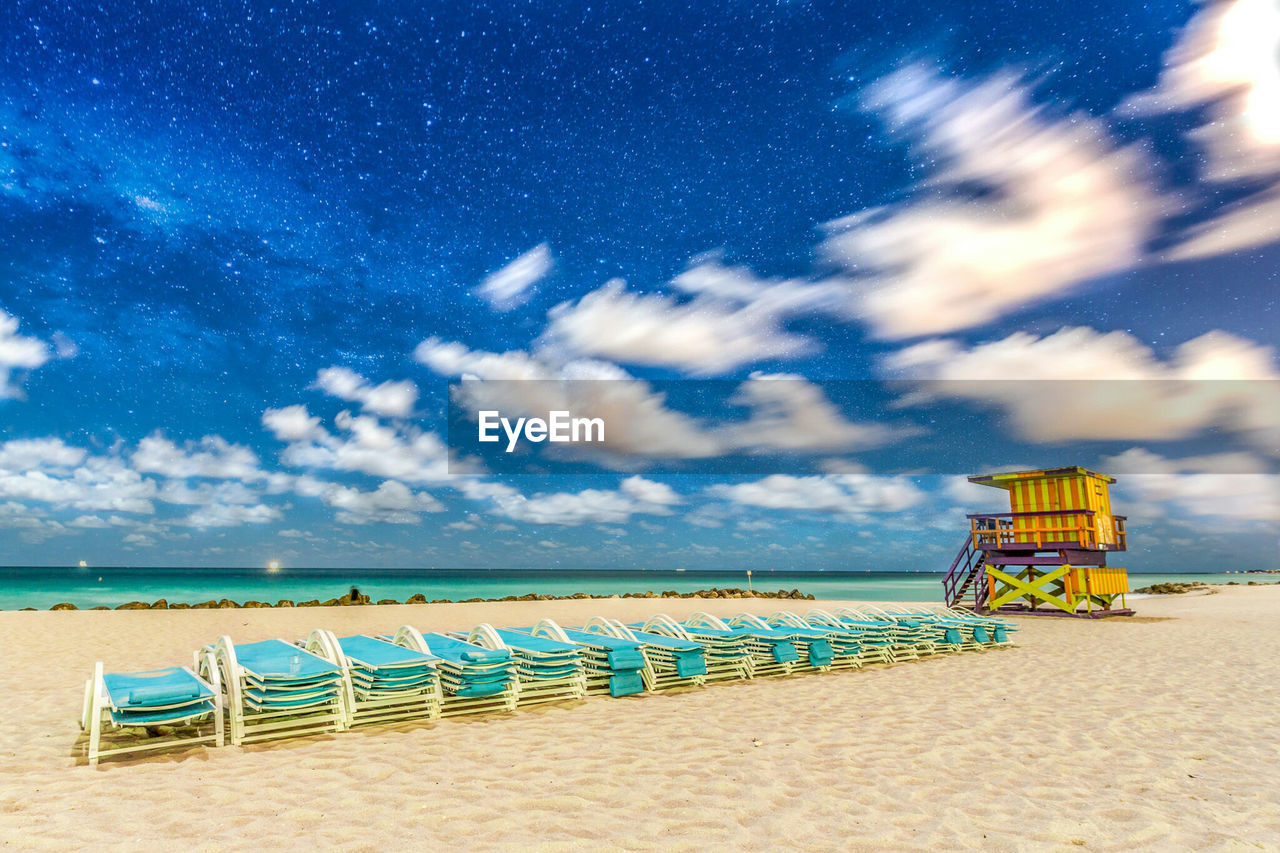 Deck chairs at beach against sky