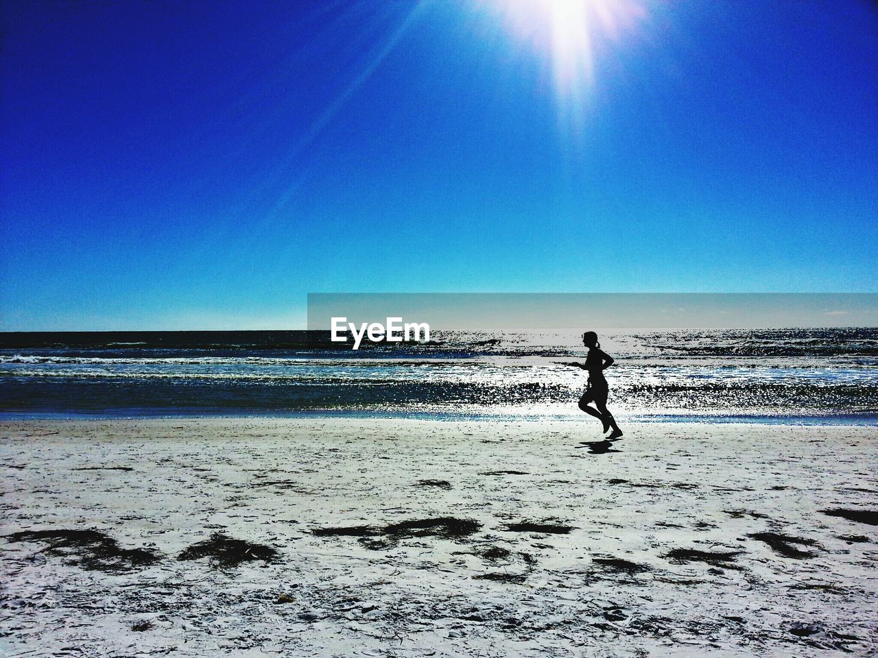 Silhouette woman running at beach against clear blue sky