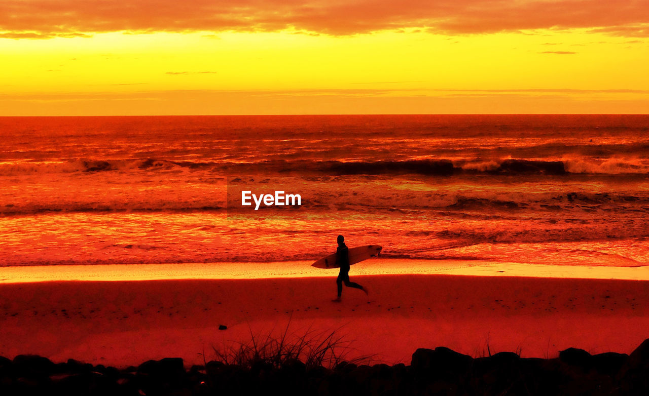 Silhouette man at beach against orange sky