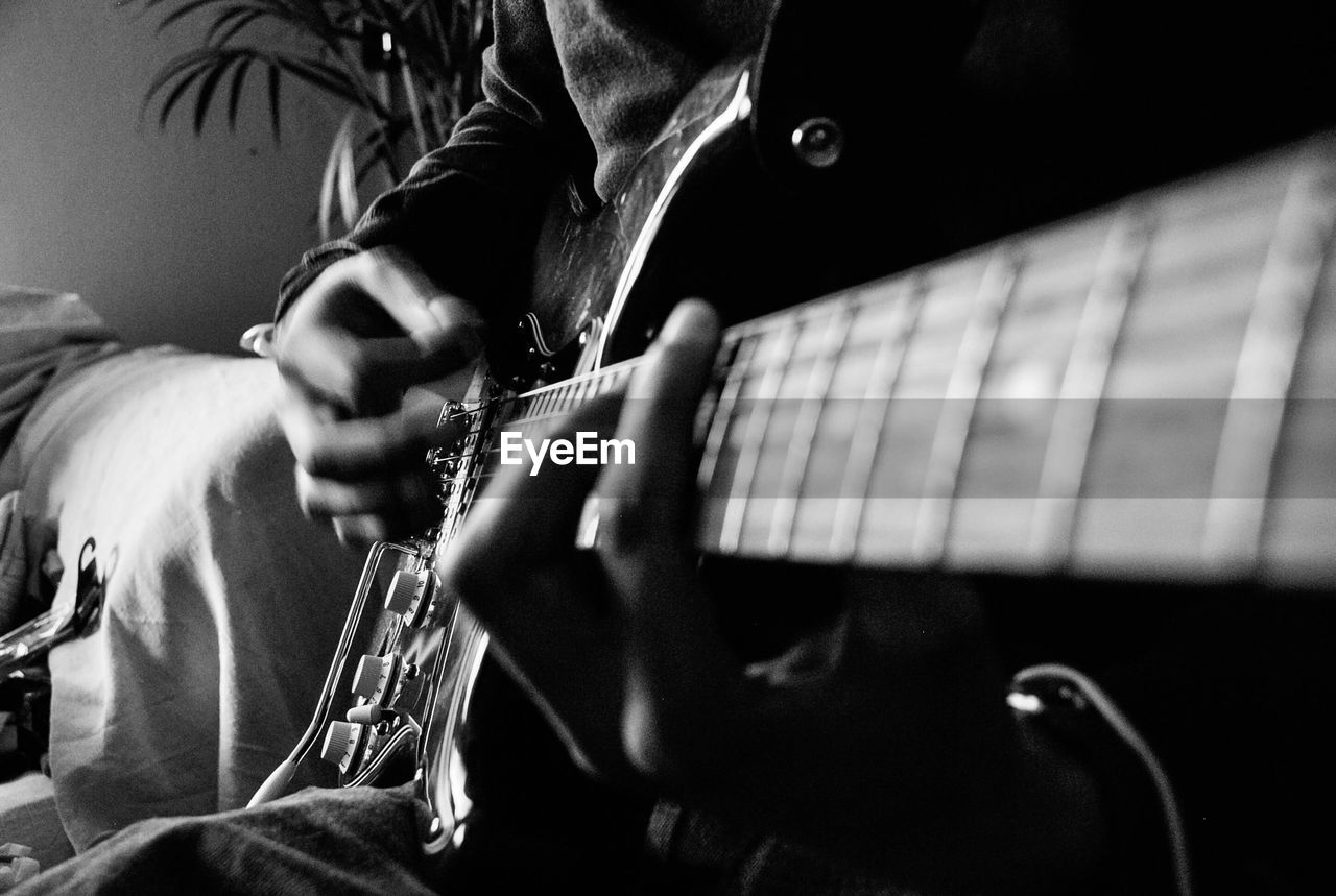 Midsection of guitarist playing electric guitar at home