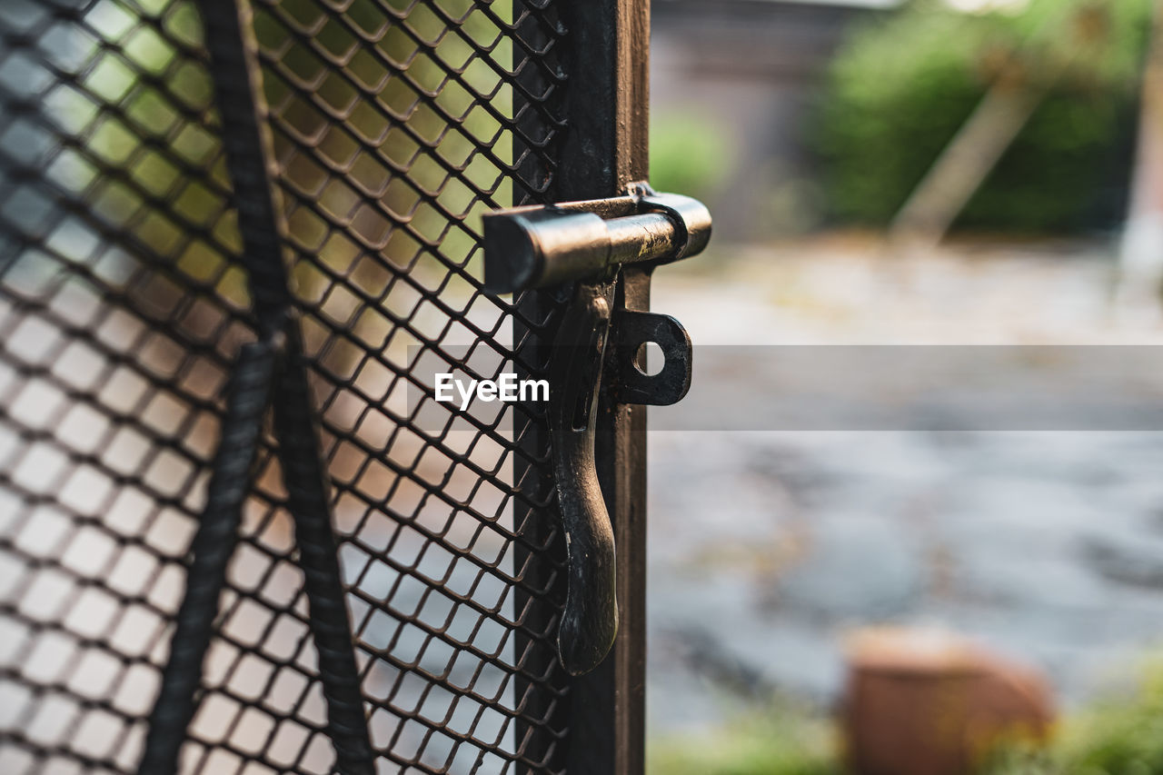 CLOSE-UP OF RUSTY METAL FENCE AGAINST BLURRED BACKGROUND