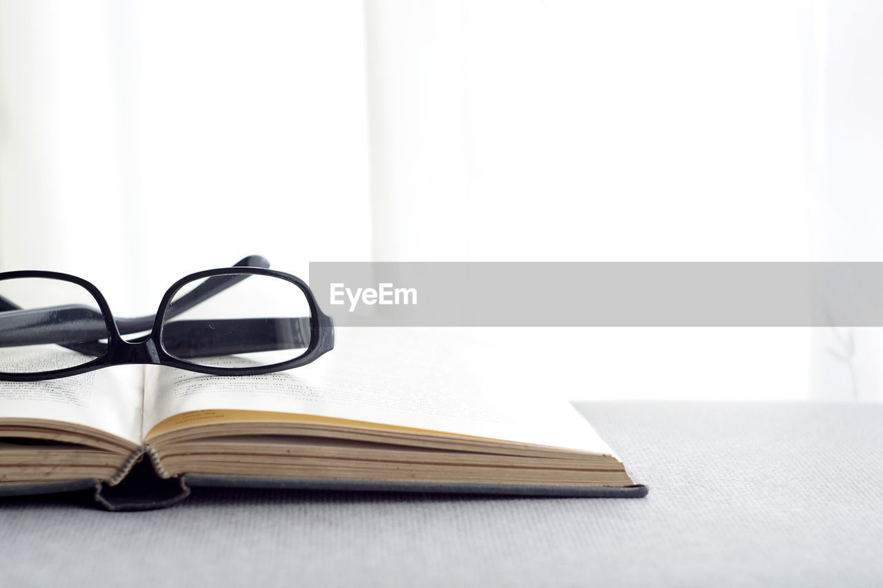 CLOSE-UP OF EYEGLASSES ON BOOK AGAINST TABLE