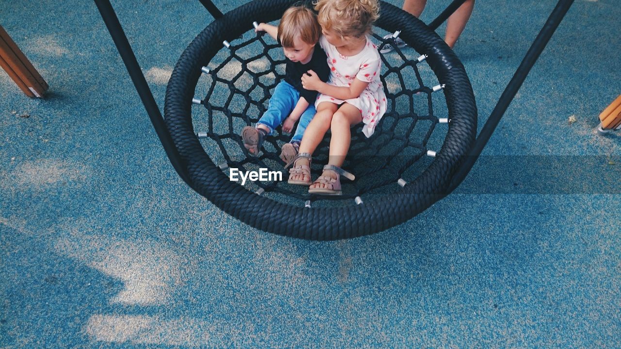 High angle view of siblings sitting on swing at playground