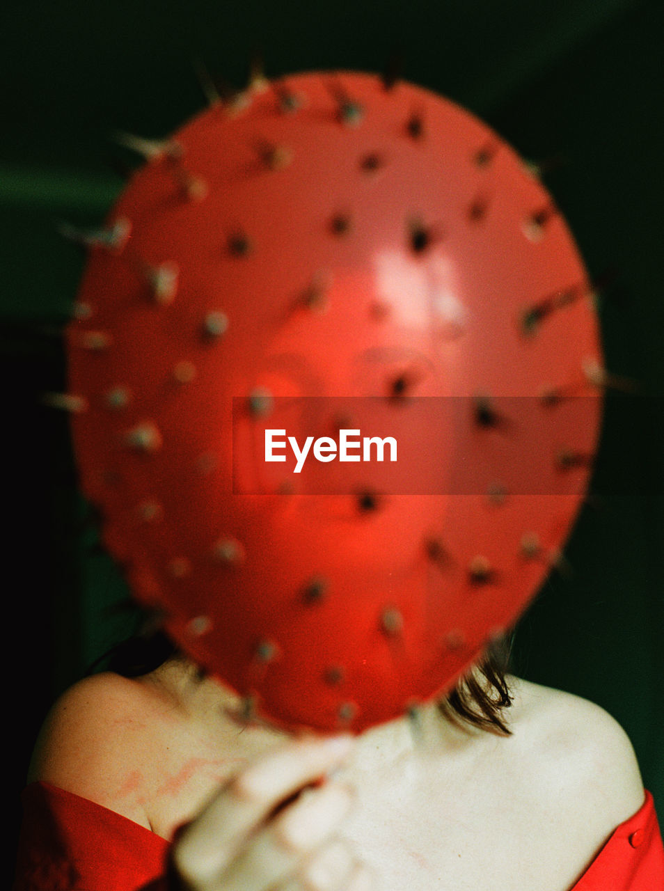 Close-up of woman holding red balloon against black background