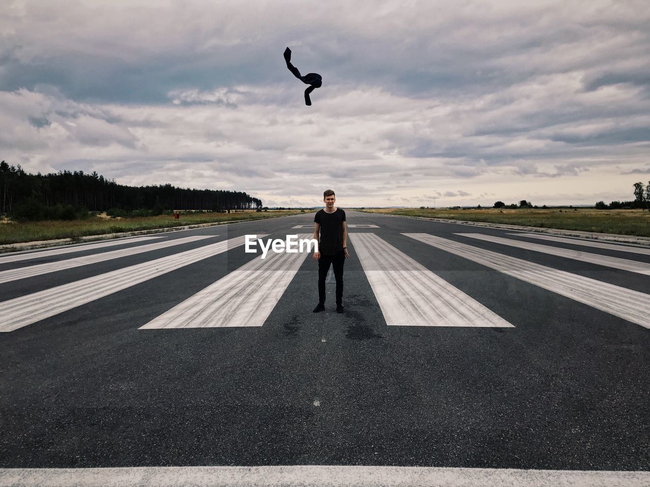 Man standing on airport runway against cloudy sky