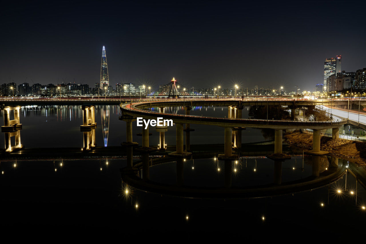 illuminated bridge over river against sky at night