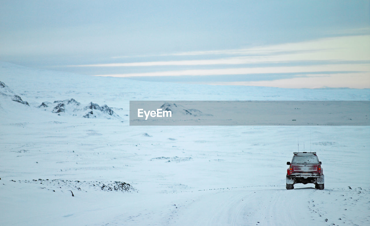 Red suv driving through winter landscape in iceland