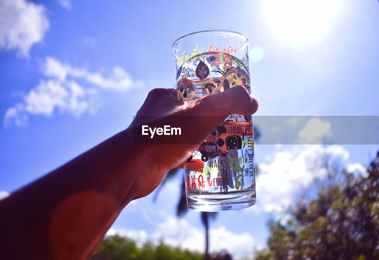 CROPPED IMAGE OF HAND HOLDING GLASS AGAINST BLUE SKY