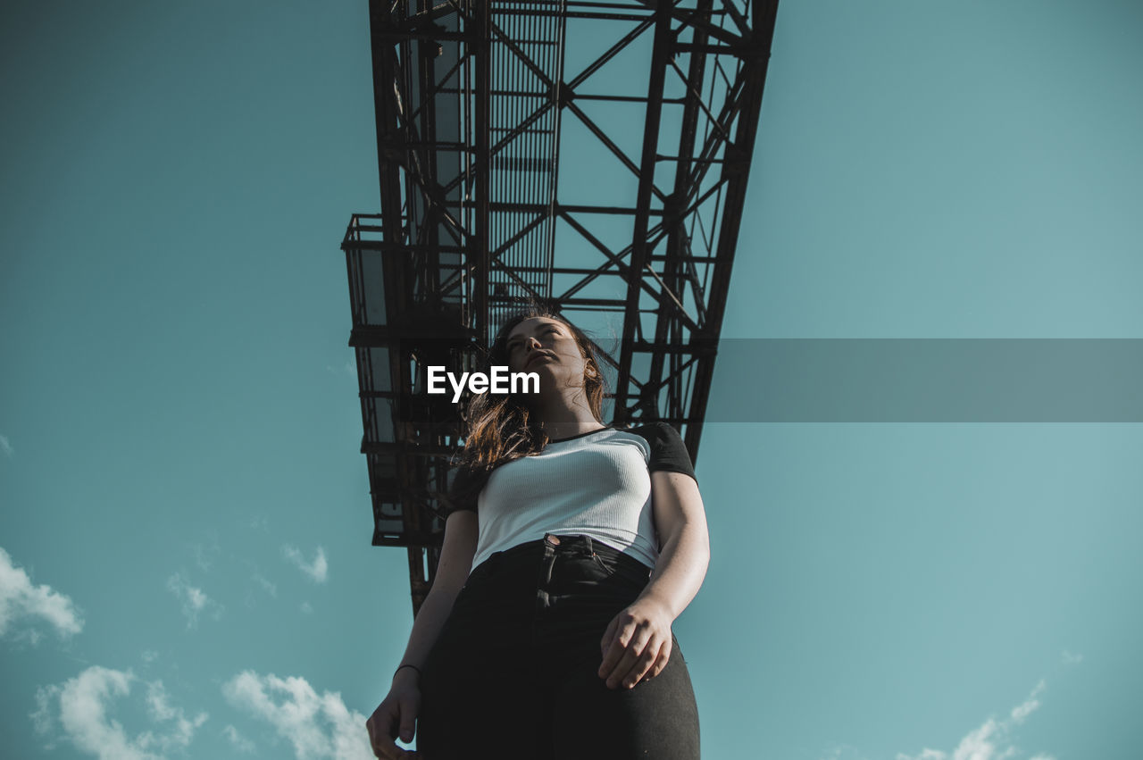 Low angle view of thoughtful young woman standing against sky