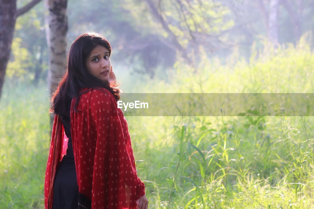 Young woman standing on field against trees