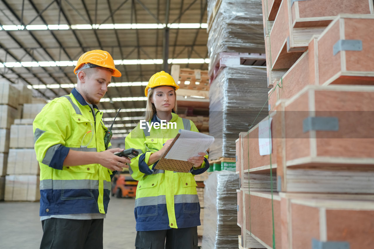 industry, occupation, hard hat, working, reflective clothing, adult, business, protection, hat, men, helmet, headwear, cooperation, teamwork, clothing, standing, warehouse, protective workwear, digital tablet, technology, manual worker, architecture, clipboard, business finance and industry, communication, two people, planning, examining, discussion, person, domestic room, distribution warehouse, holding, list, security, indoors, construction industry, checklist, coworker, building, talking, freight transportation, computer, engineering, wireless technology, looking, mature adult, three quarter length, construction worker, paper, factory, construction site, occupational safety and health, young adult, shipping, expertise, togetherness, plan, meeting, looking down, building contractor, blueprint, box, showing, document, explaining