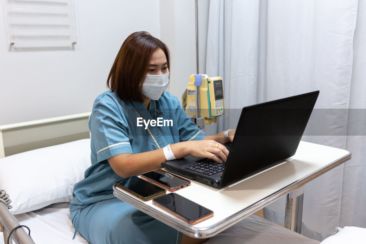 Illness asian patient women still  using laptop for working hard  in patient room of hospital